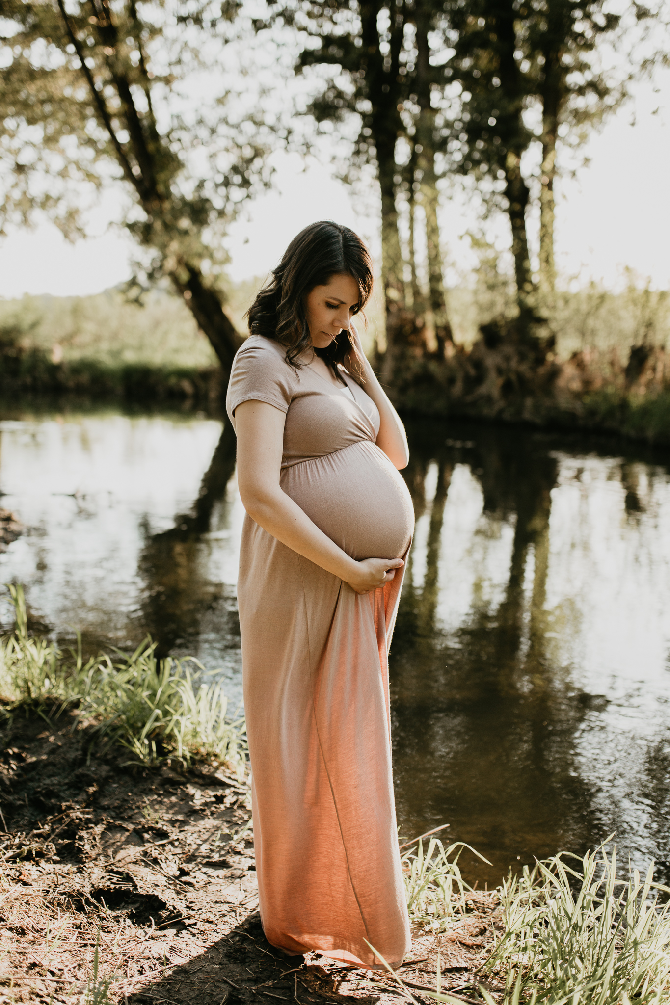 Expecting mother by the creek looking down at her belly.
